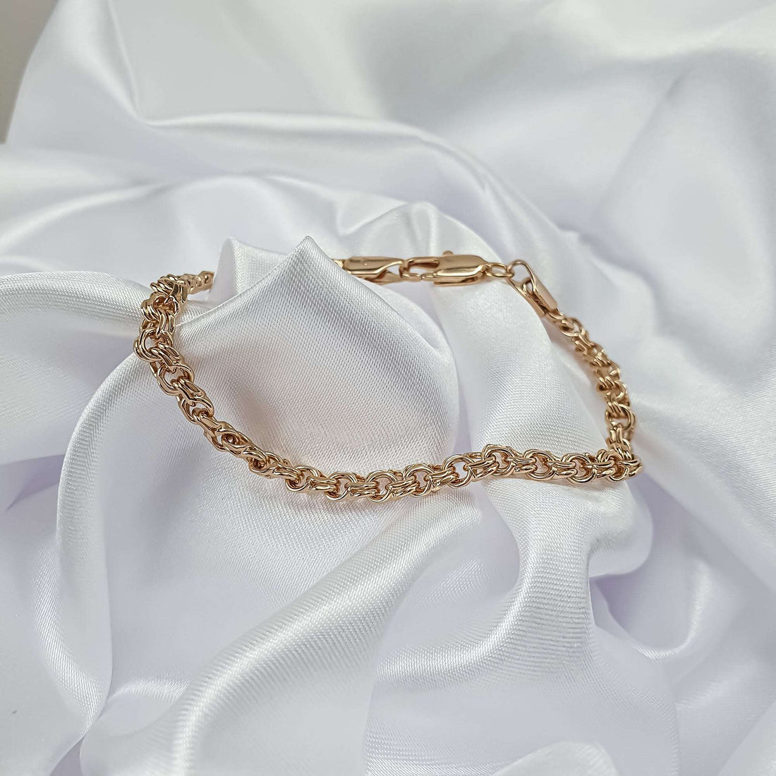 Fine gold-plated woven bracelet on white silk, lobster clasp in view