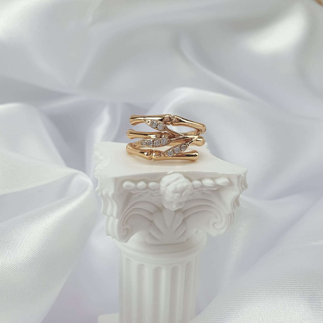 Three-band leaf ring with cubic zirconia inserts on a white antique pedestal