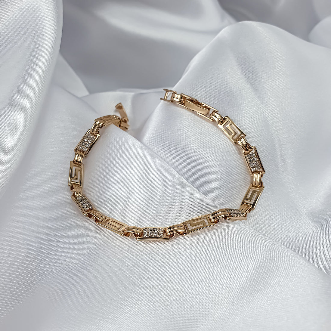 Greek key bracelet with cubic zirconia laid in an arc on white silk