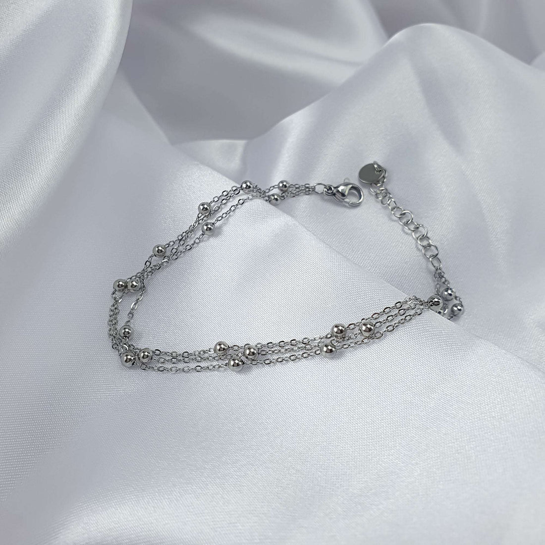 Silver-tone layered bracelet with shiny beads on white silk fabric
