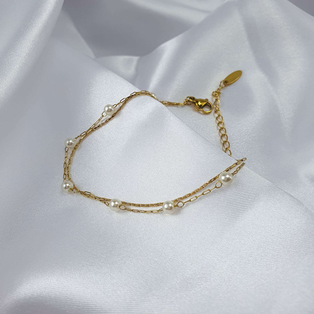 Delicate two-strand bracelet with small pearls and gold-tone chains on white silk