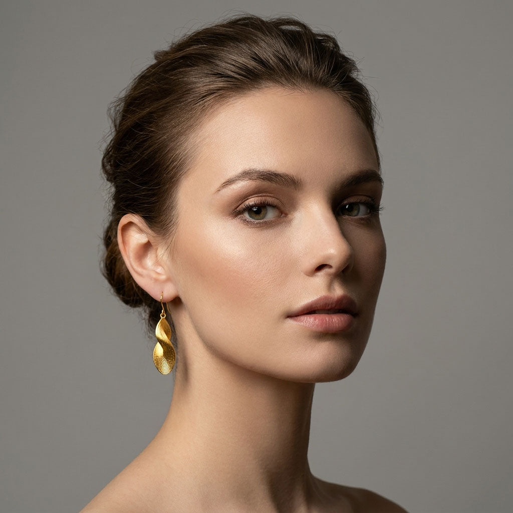 Model wearing long wavy gold-plated earrings that frame the neck and profile