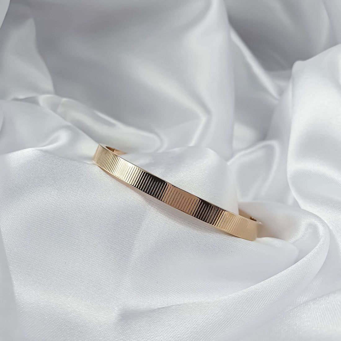 Ribbed gold-plated bangle close up on white silk, fine stripes shining