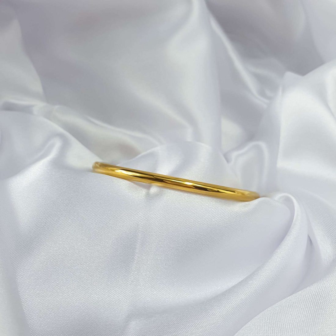 Classic gold-tone bangle on white silk showing its thin round profile