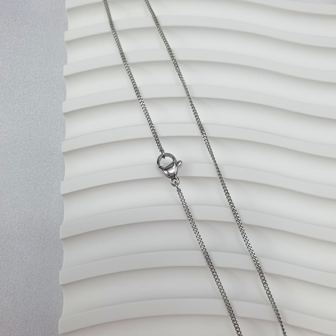 Shiny silver-tone steel curb chain on a wavy white surface