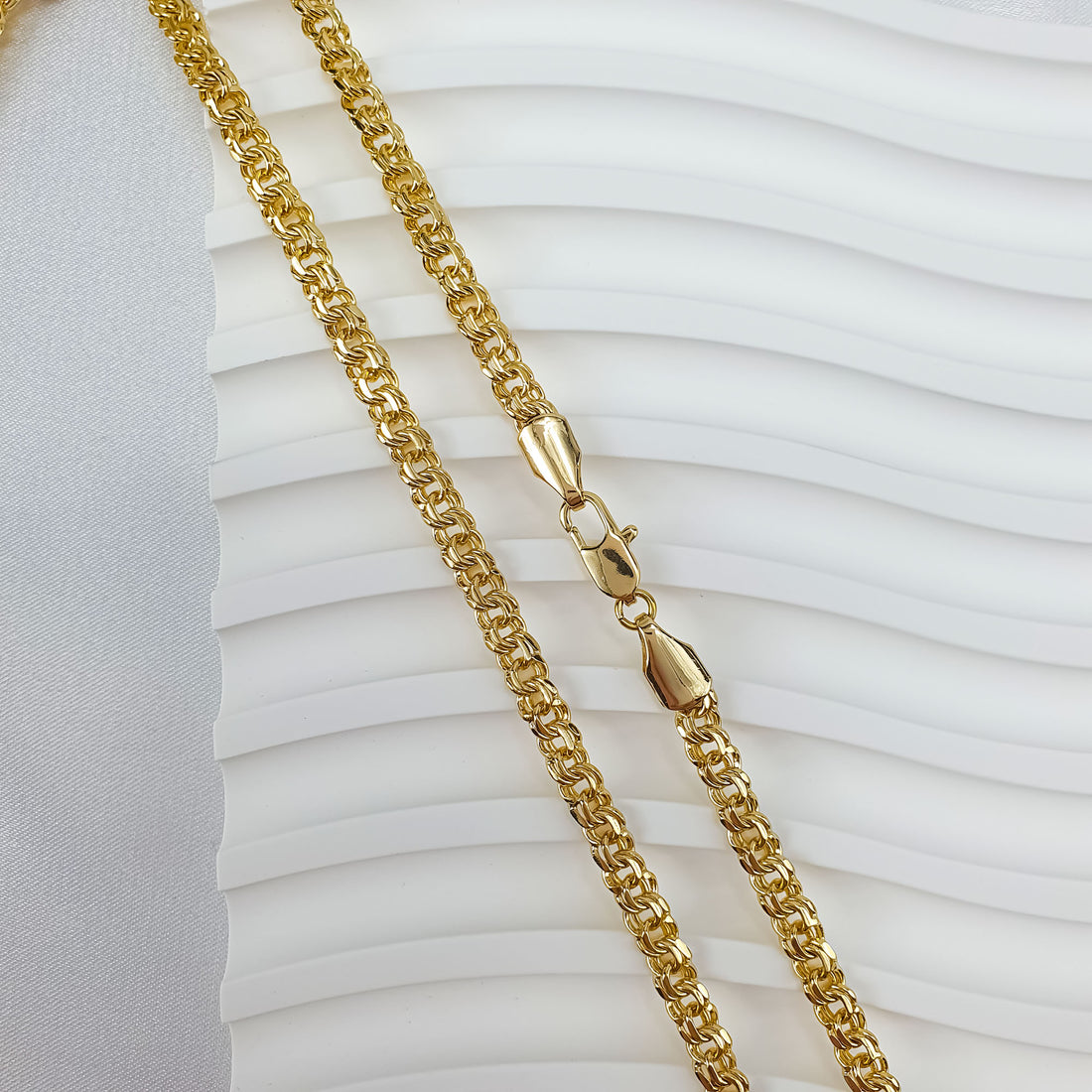 Gold-tone Garibaldi chain on a white wavy background, lobster clasp close up