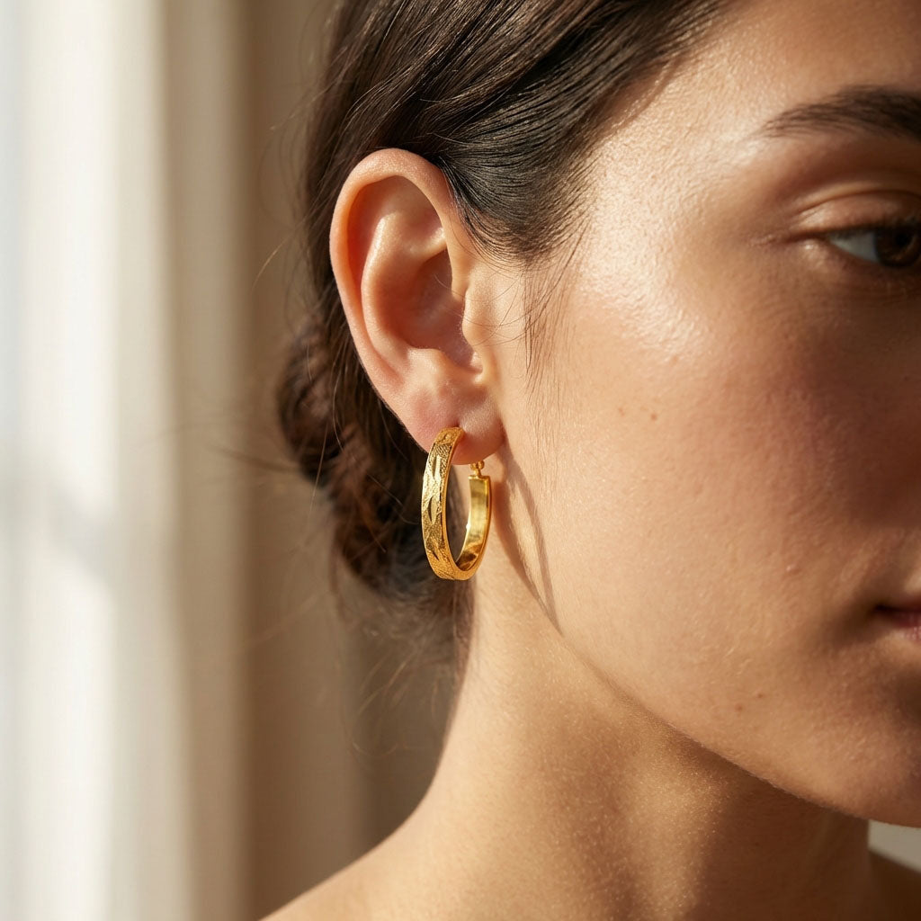 Close-up of an engraved gold-tone hoop earring on a model's ear, daylight