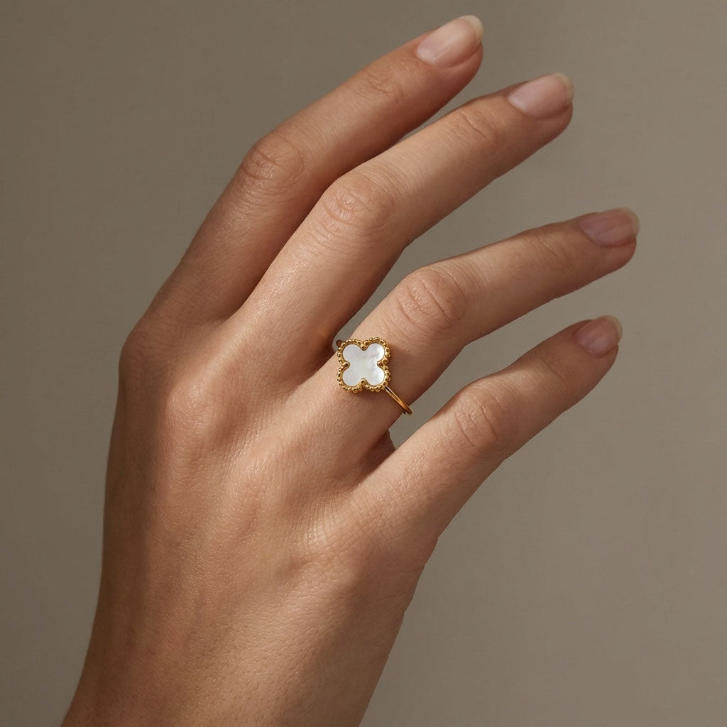 Four-leaf clover ring on a woman's finger, gold-tone edge glowing in warm light