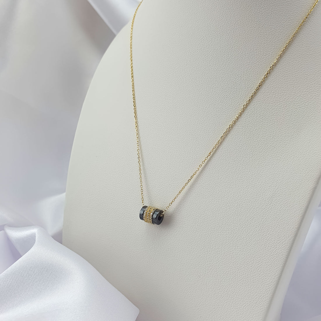 Black cylinder pendant necklace on a light jewellery stand with silk