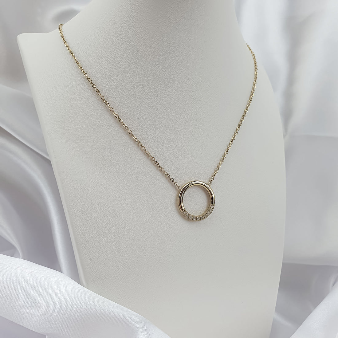 Gold-plated circle necklace on a white bust, stones sparkling along the lower edge