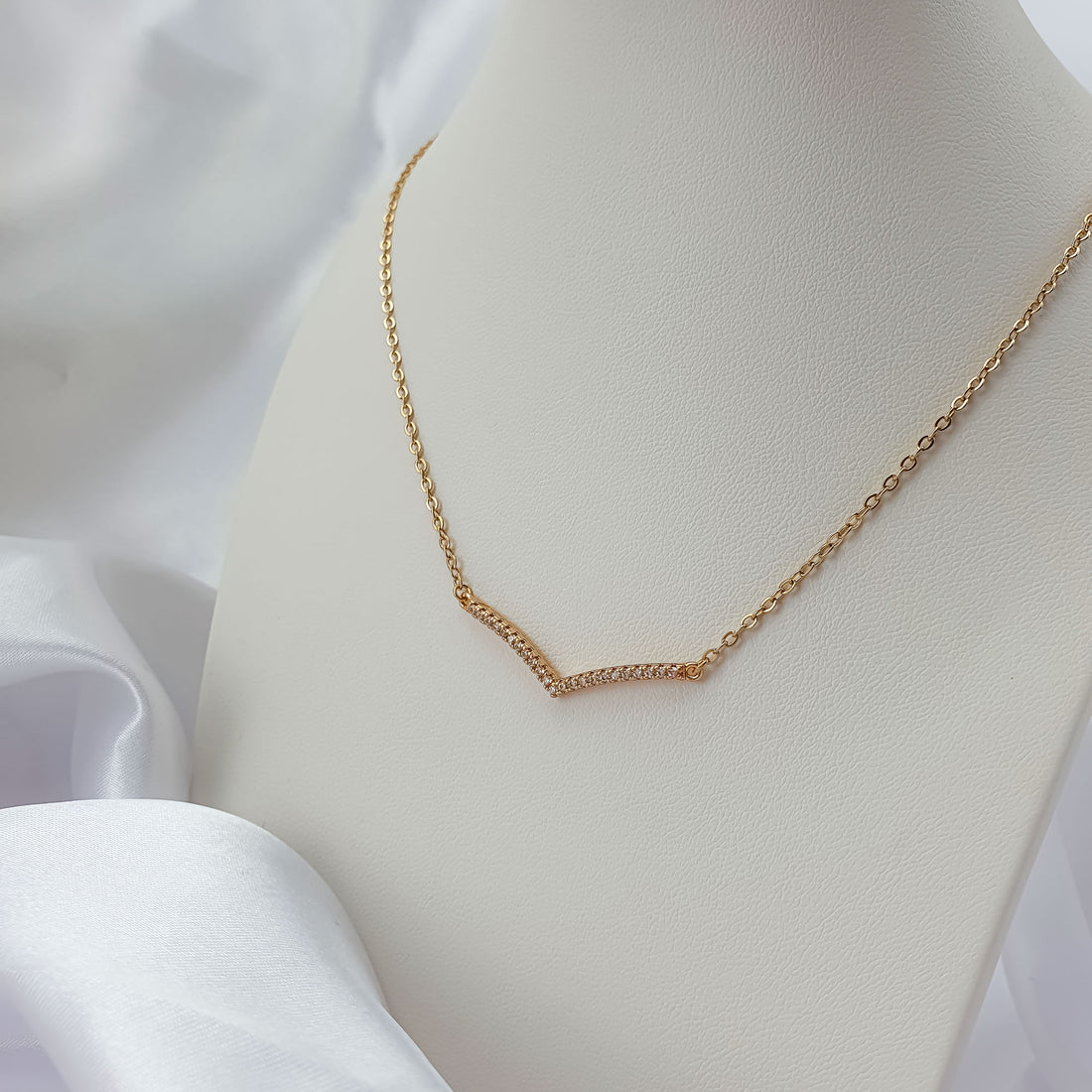 Delicate V-shaped necklace with cubic zirconia on a white bust, chain close-up
