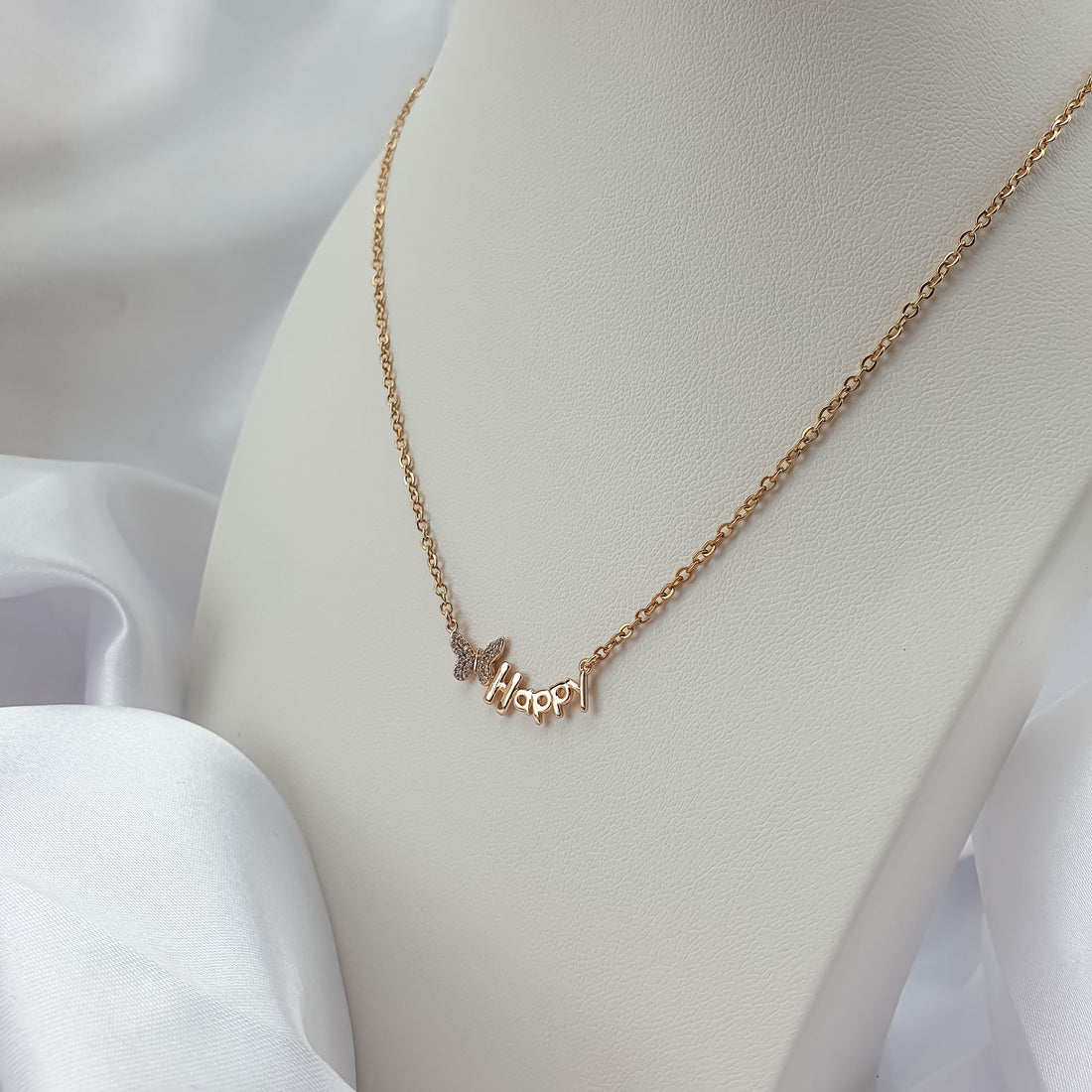 Gold-plated Happy necklace with a stone-set butterfly on a white bust, close-up