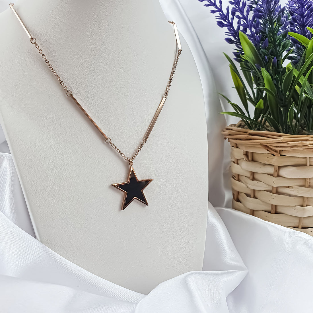 Black star pendant on a rose gold-tone chain on a white jewellery bust