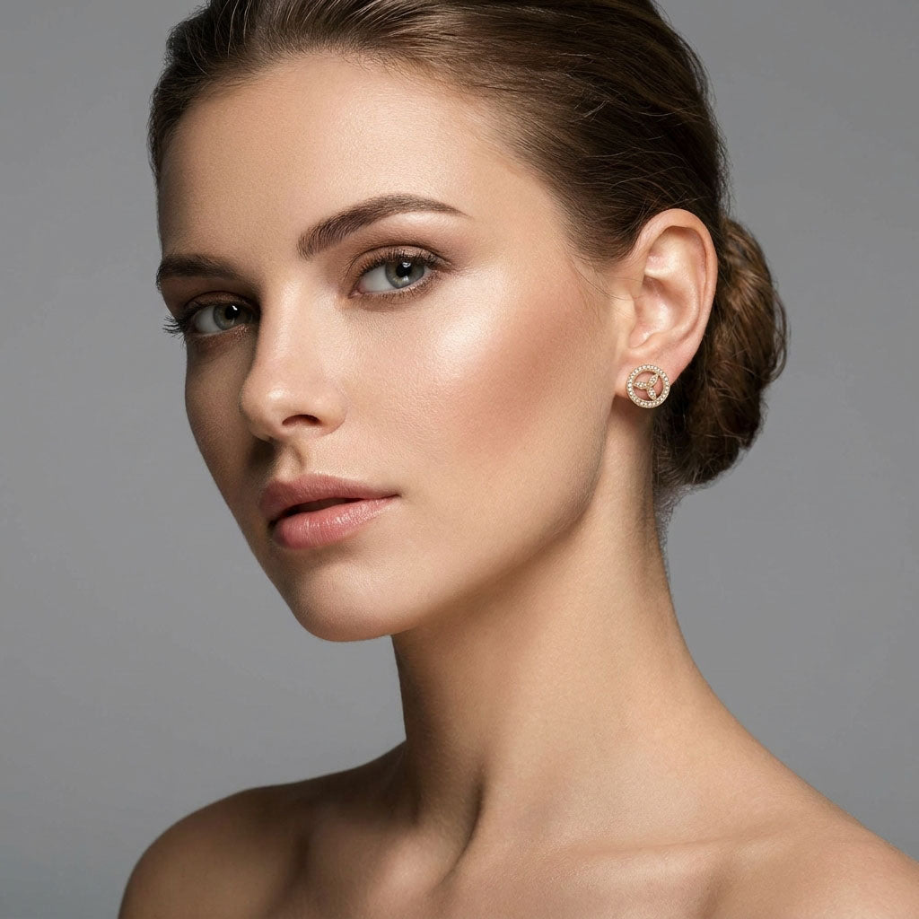 Round gold-tone stud with a cubic zirconia border worn in a woman's ear
