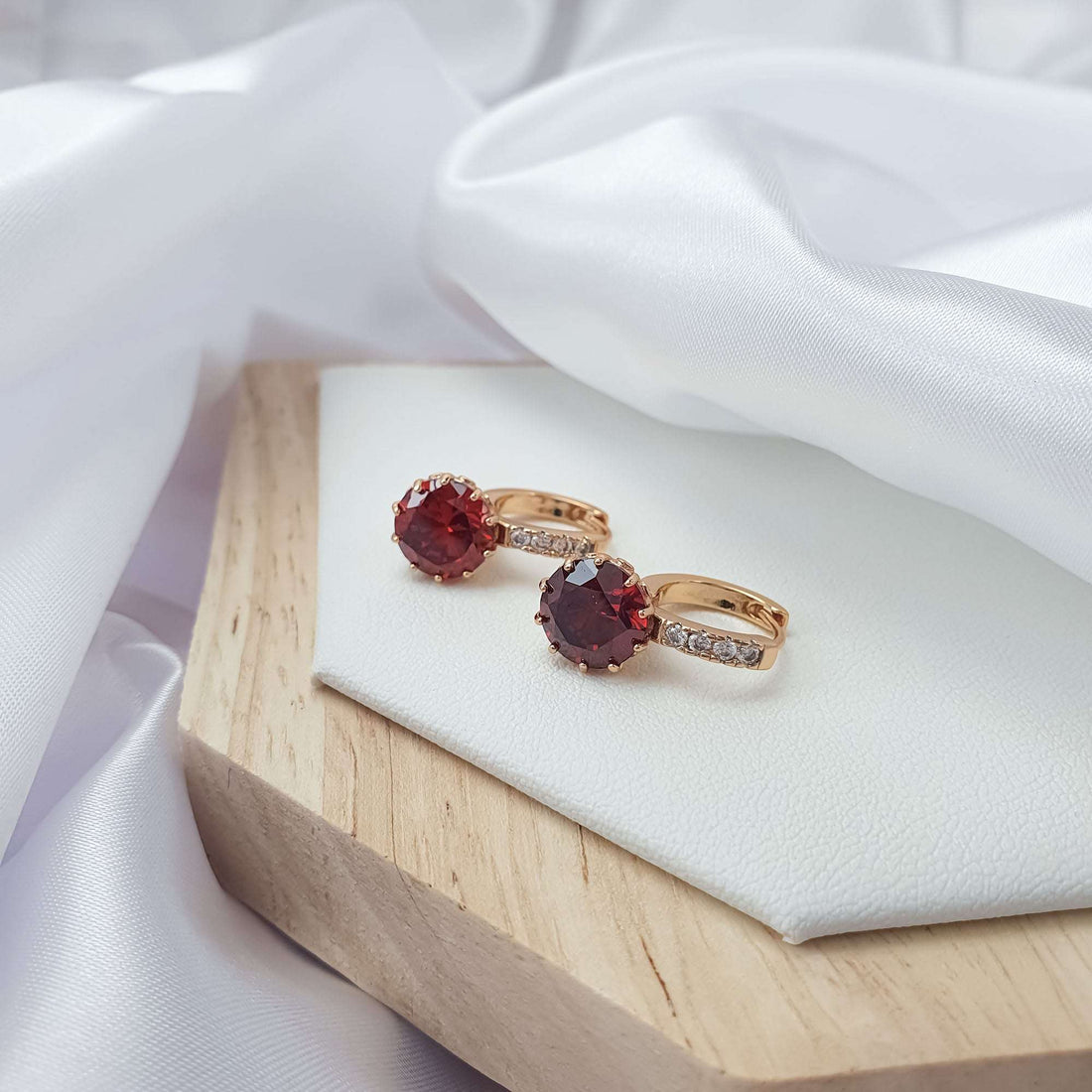 Hoop earrings with dark red stones on a white tray, showing the closure