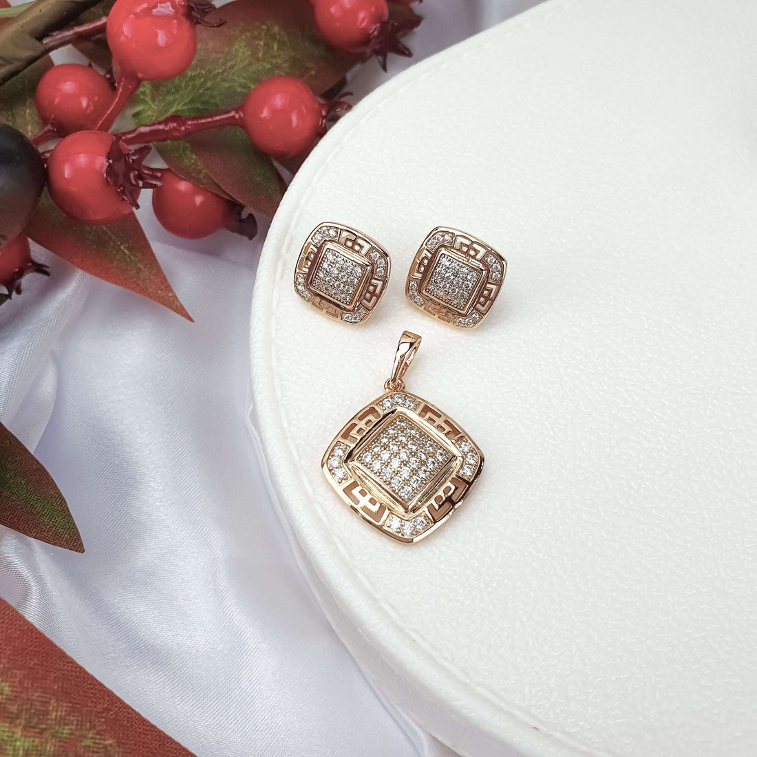 Gold-plated Greek key set with cubic zirconia on a white box beside red berries