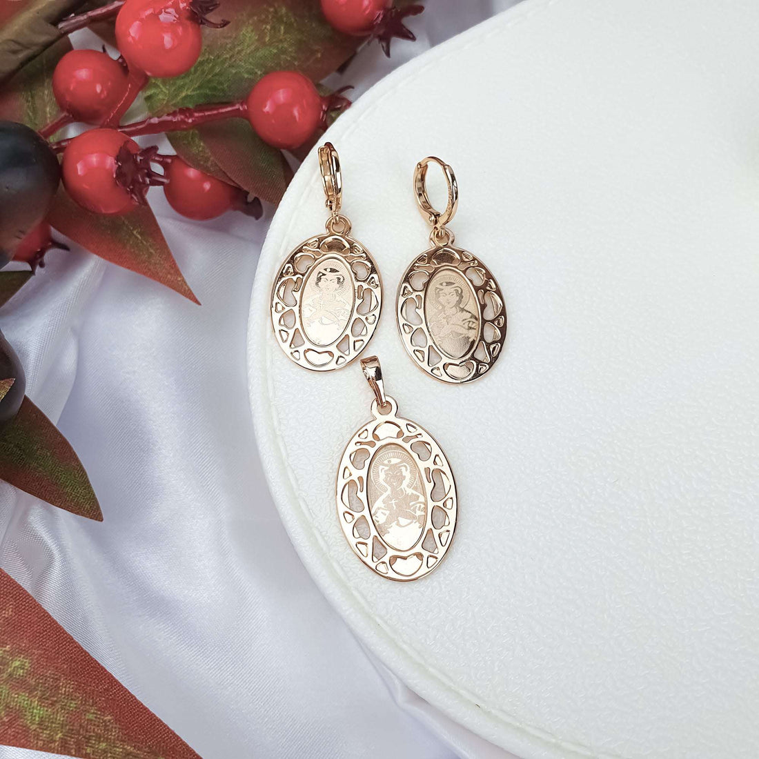 Gold-plated Virgin Mary medallion set on a white jewellery box with red berries