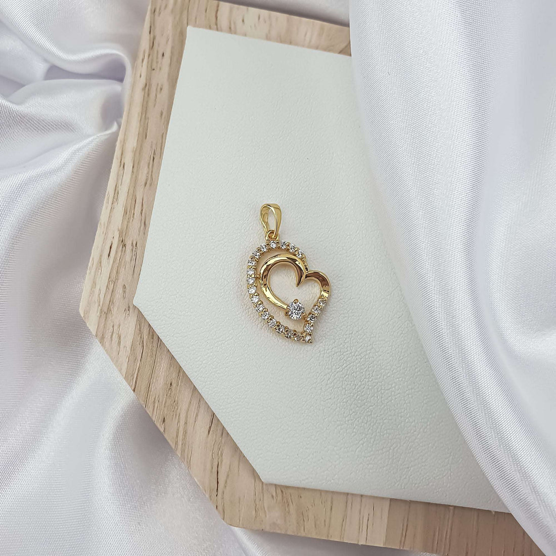 Cubic zirconia heart pendant on a light leather tray in a wooden frame