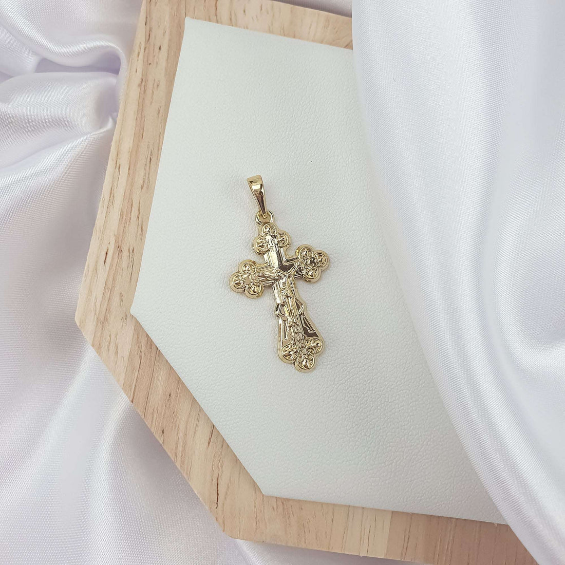 Gold-plated cross with a raised crucifix and flower-shaped ends on a wooden board