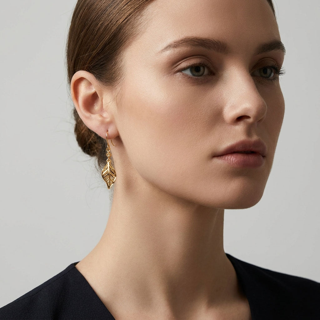 Gold-plated leaf earring on a model's ear, side view, light grey background