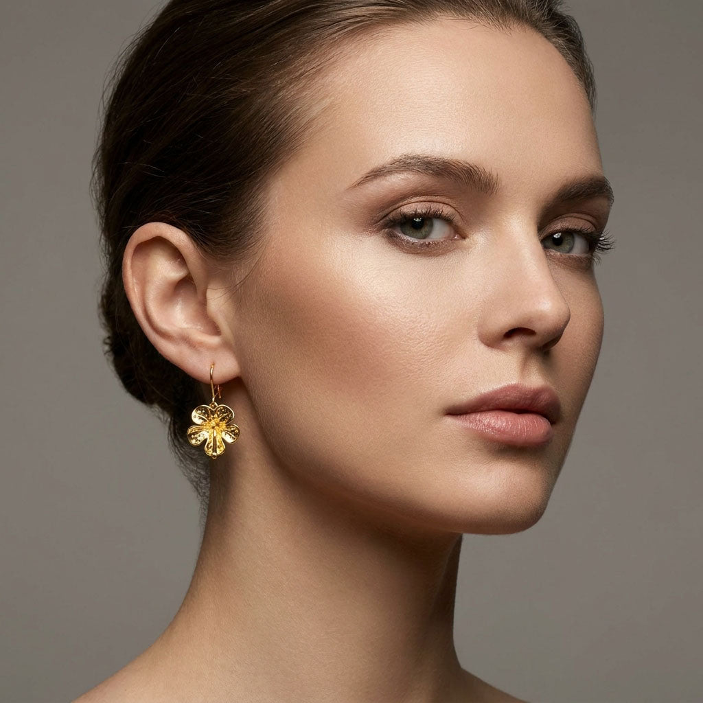 Gold-plated flower earring with a hook fastening worn by a model, close-up