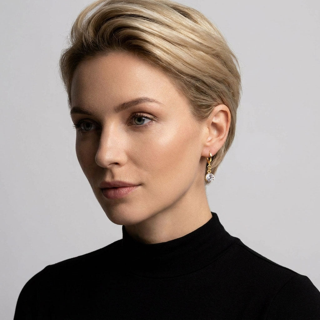 Gold-plated drop earring with a white stone on a blonde model's ear