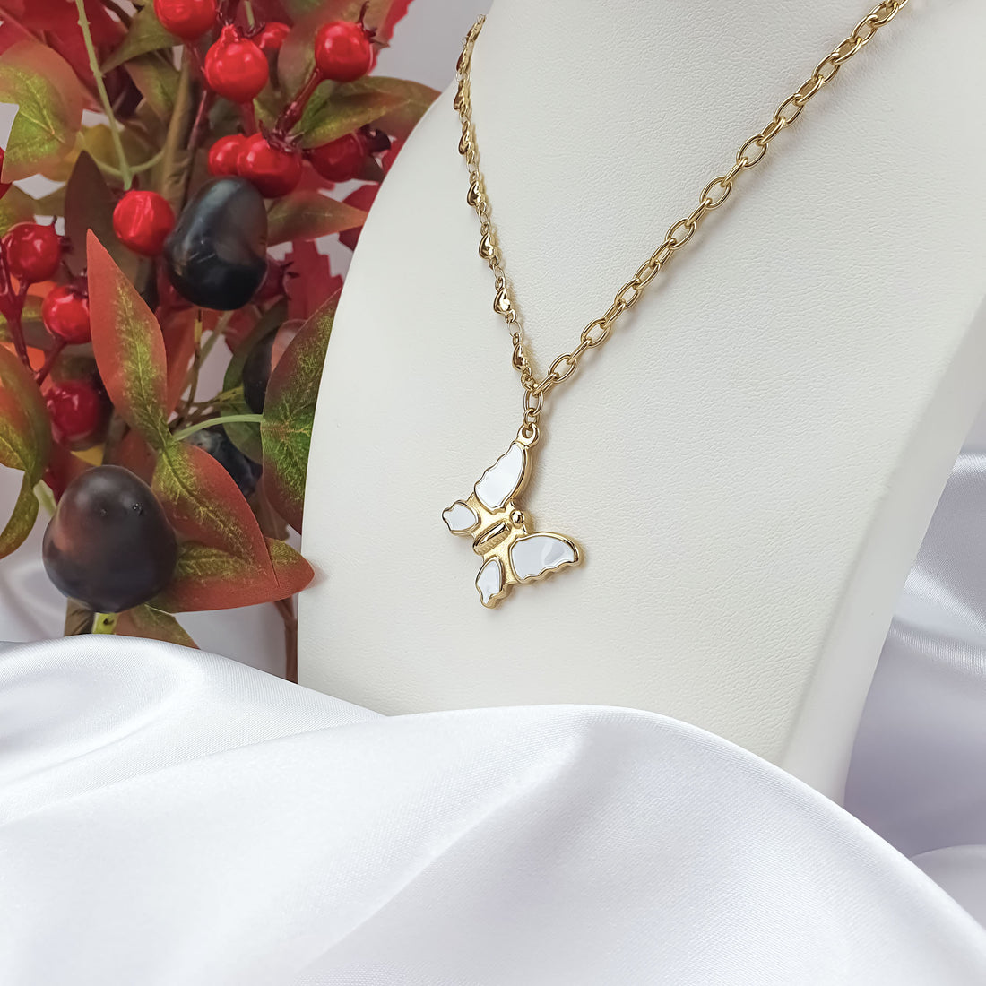 Gold-plated enamel butterfly pendant on a white jewellery bust with berries