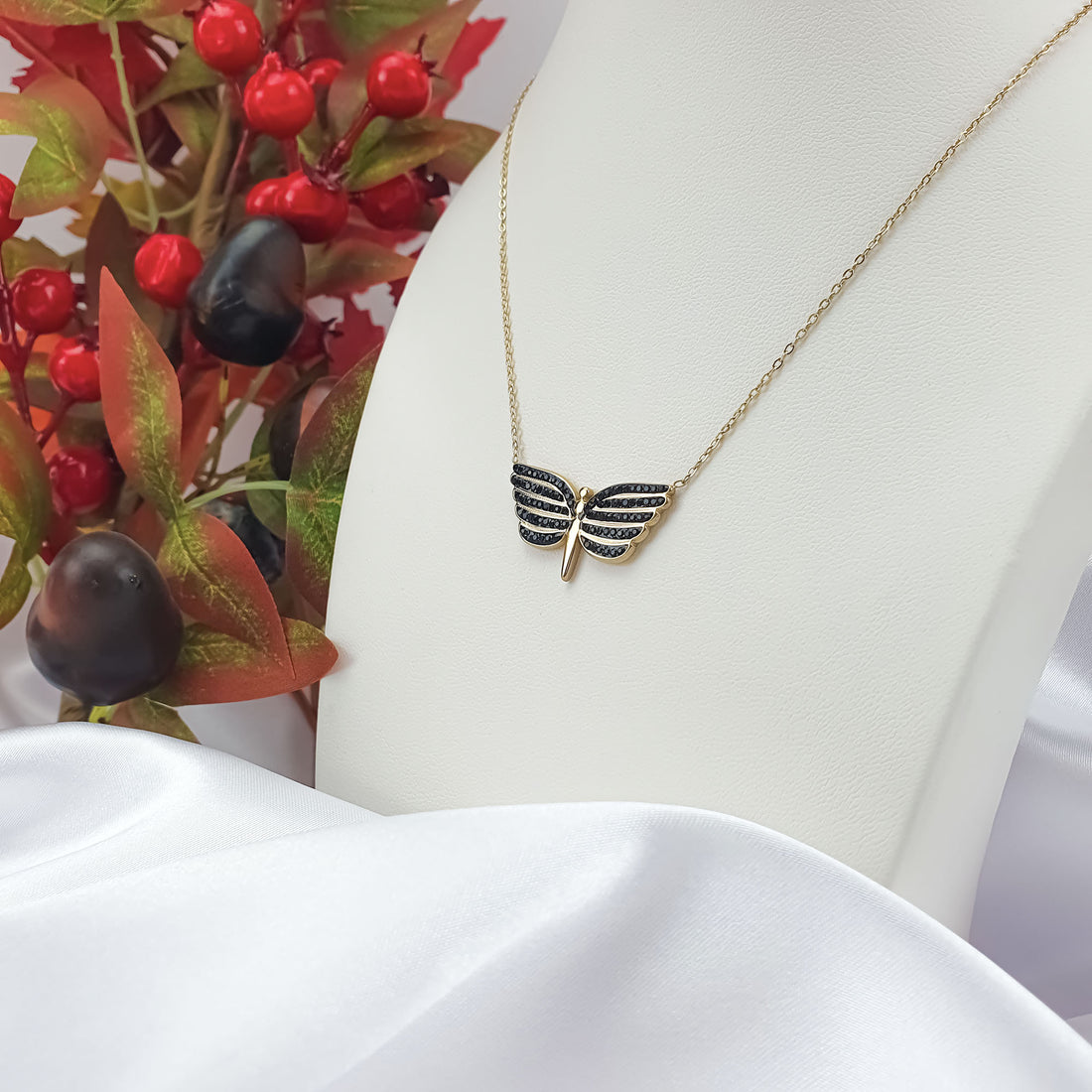 Gold-plated butterfly necklace on a white display bust among red decorative berries
