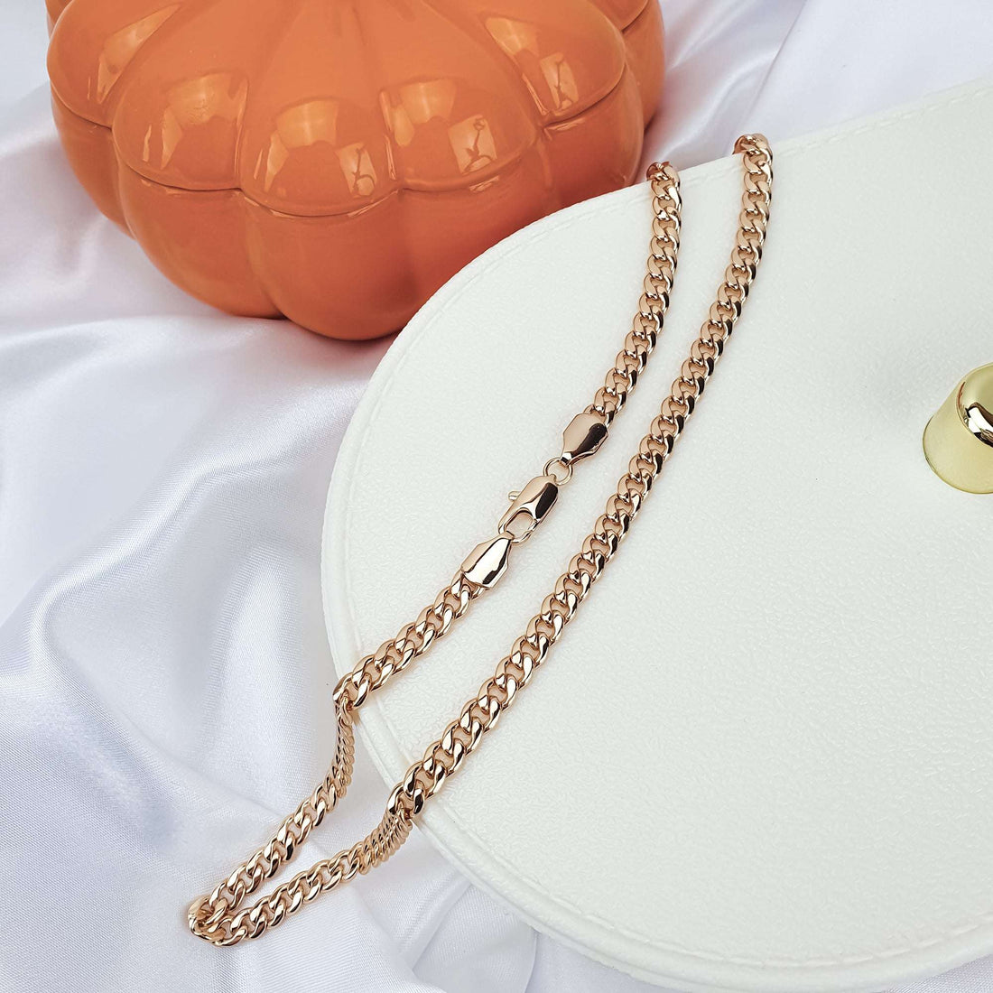 Unisex gold-plated curb chain on a light tray by a pumpkin box