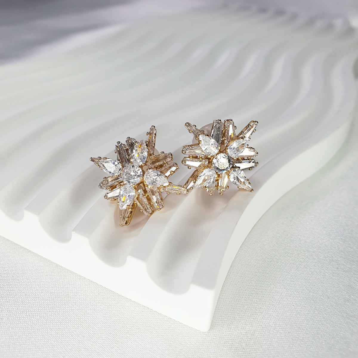 Gold-tone star clip-on earrings at an angle on a white stand