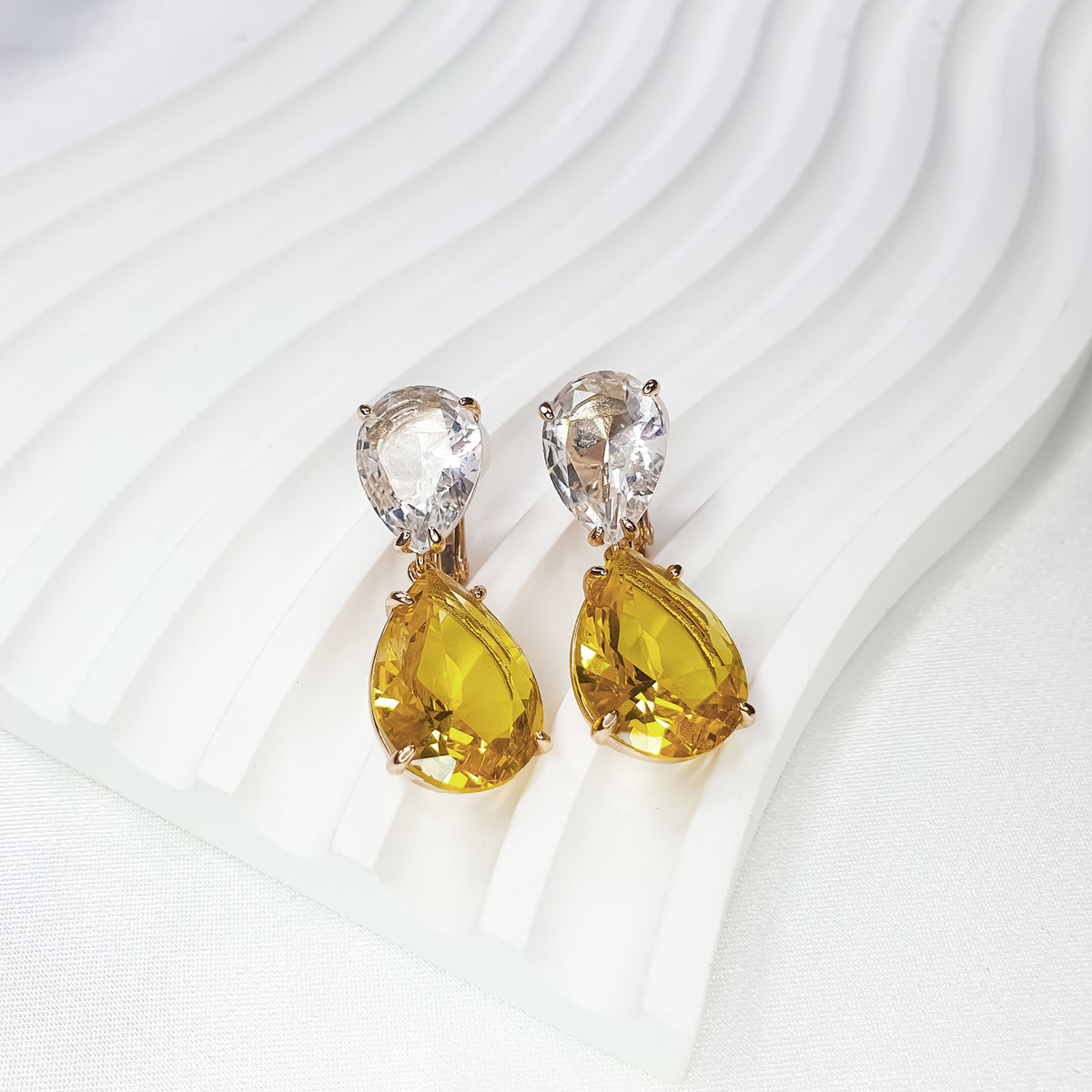 Clip-on earrings with yellow cubic zirconia on a white stand, clip visible