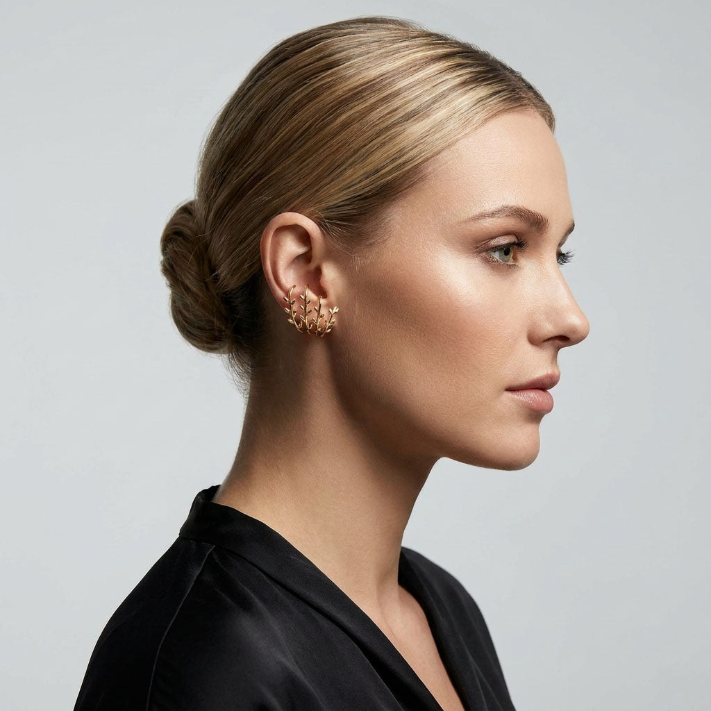 Gold-tone leaf sprig earrings on a model, fair hair up, black outfit