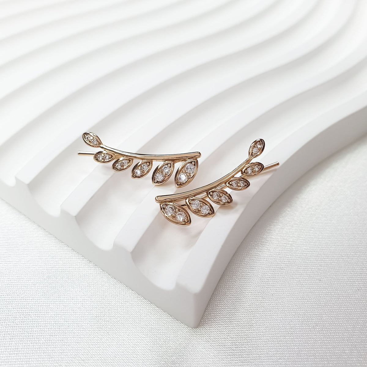 Pair of leaf branch earrings with cubic zirconia on a ribbed ceramic stand