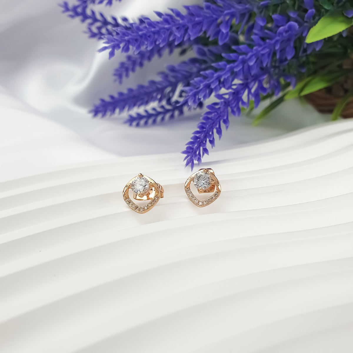 Small gold-plated earrings with clear cubic zirconia beside lavender flowers