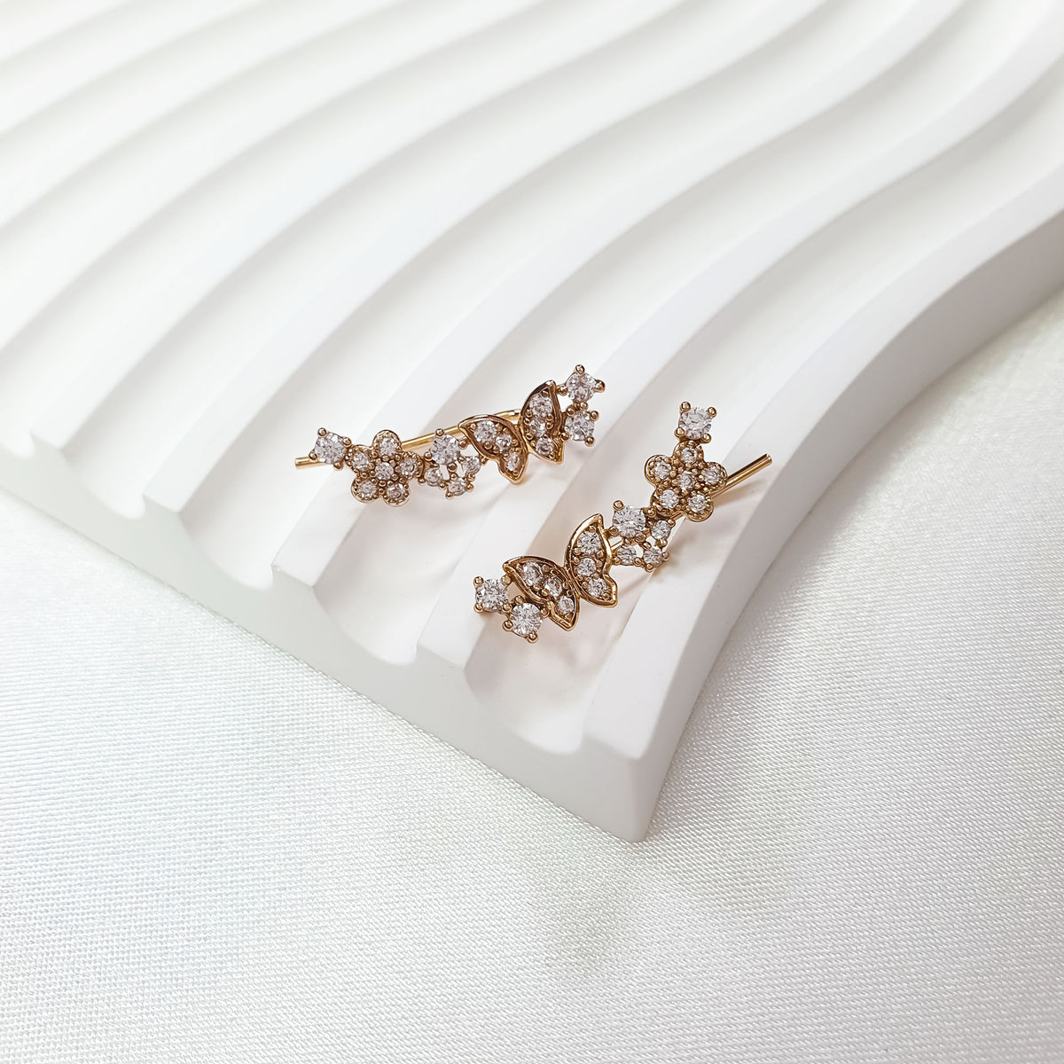 Close-up of flower and butterfly earrings on a white ribbed ceramic stand