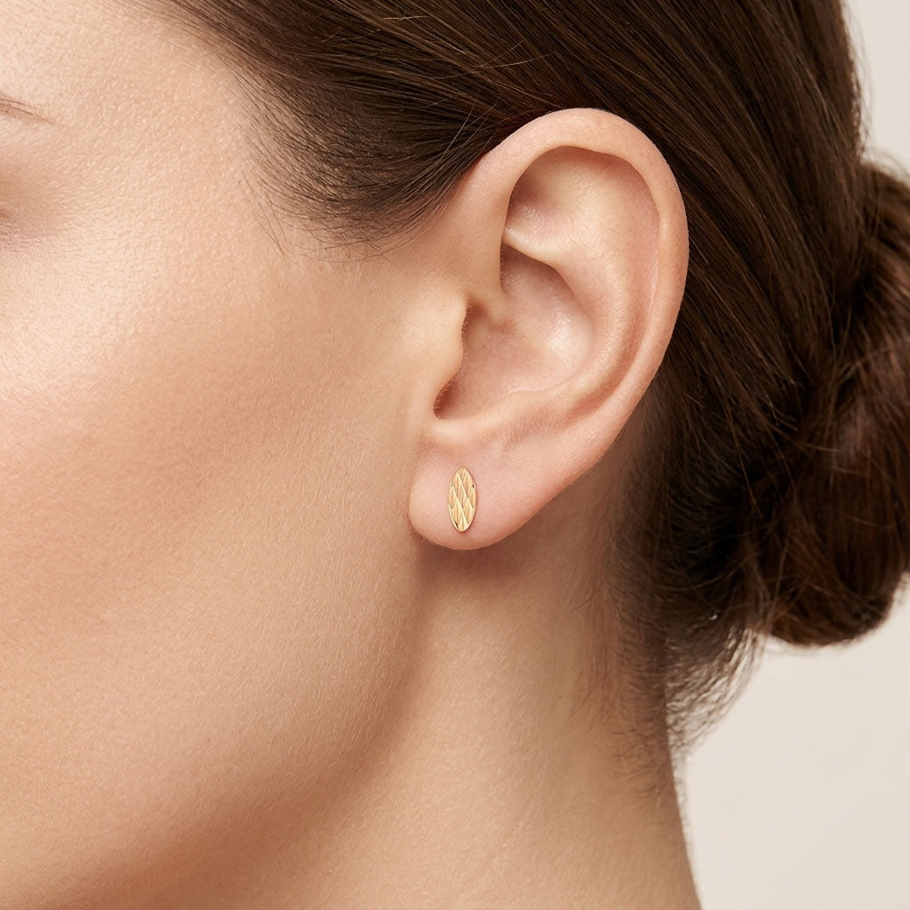 Close-up of a gold-plated oval stud with a rhombus pattern on the ear