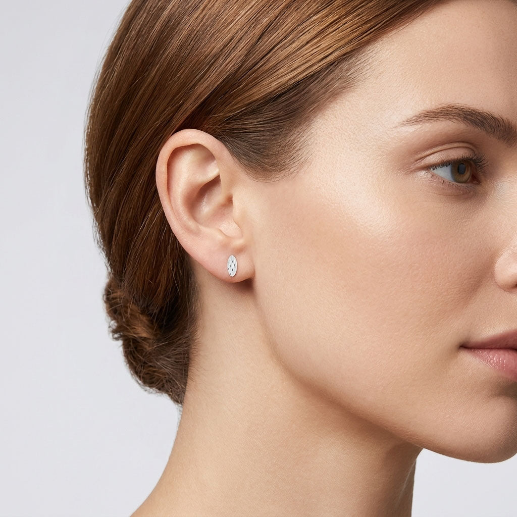 Silver-tone oval stud earring with a relief pattern on a model's ear