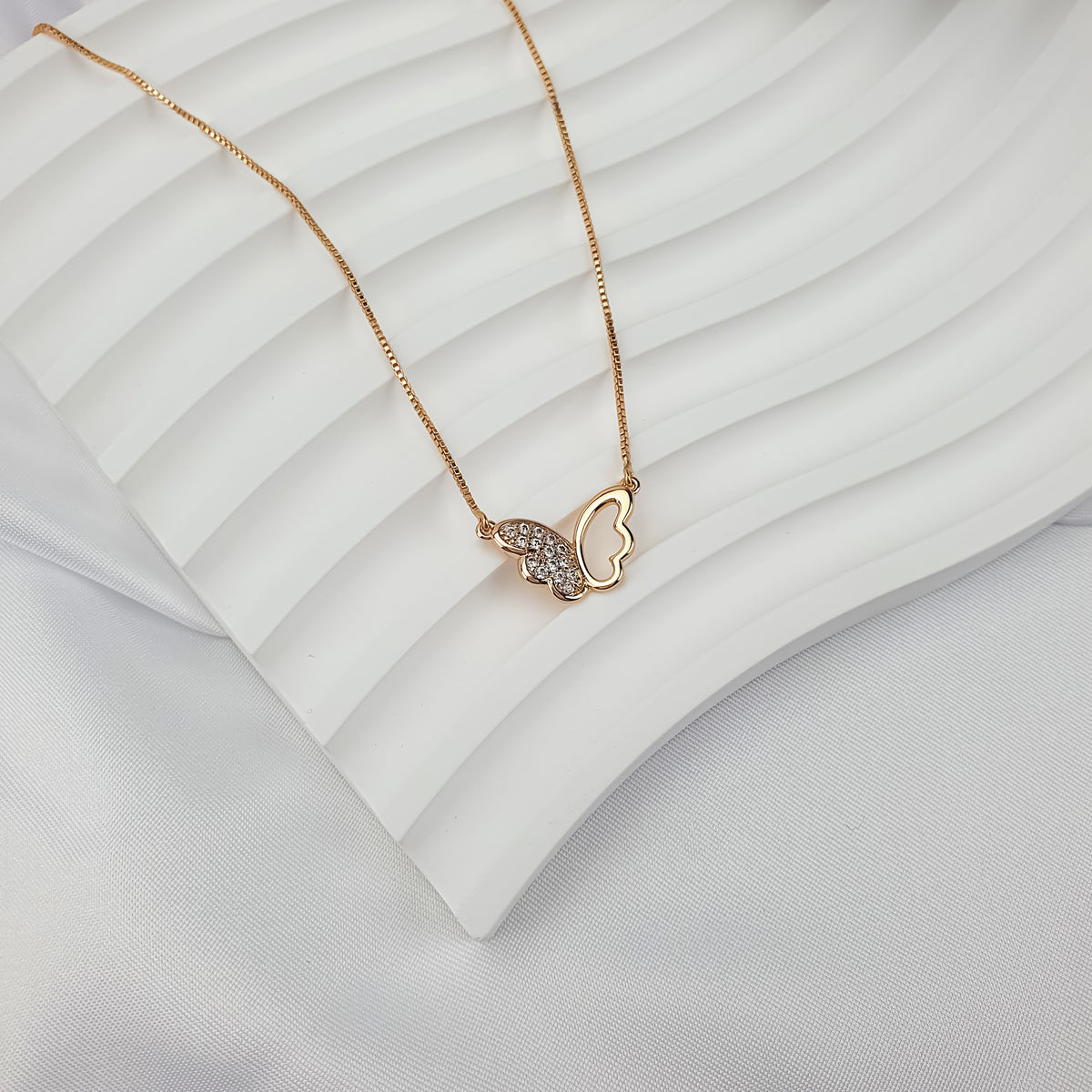Gold-plated butterfly pendant with a cubic zirconia wing on a wavy white ceramic tray