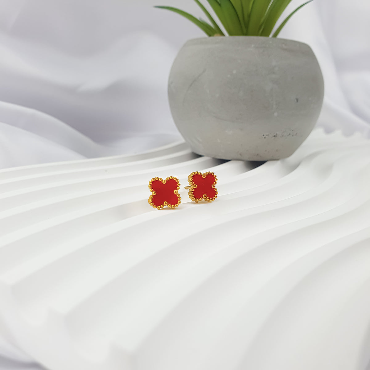 Red clover studs with visible posts on a white ribbed stand beside a plant