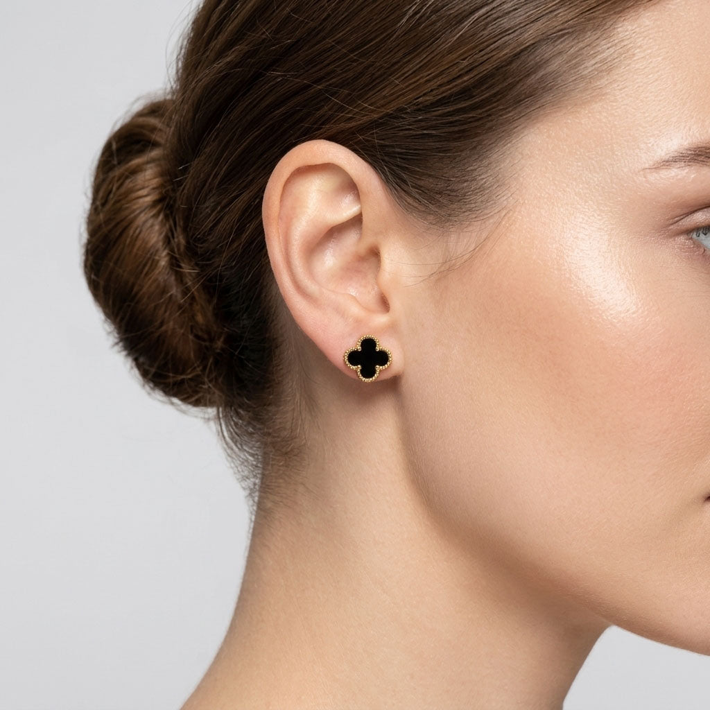 Black enamel clover stud with a gold-tone beaded border in a woman's ear