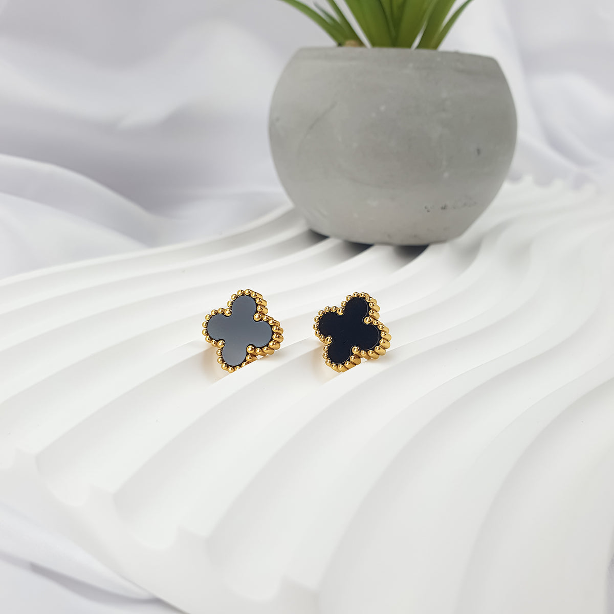 Two gold-tone clover earrings in black and white enamel on white fabric