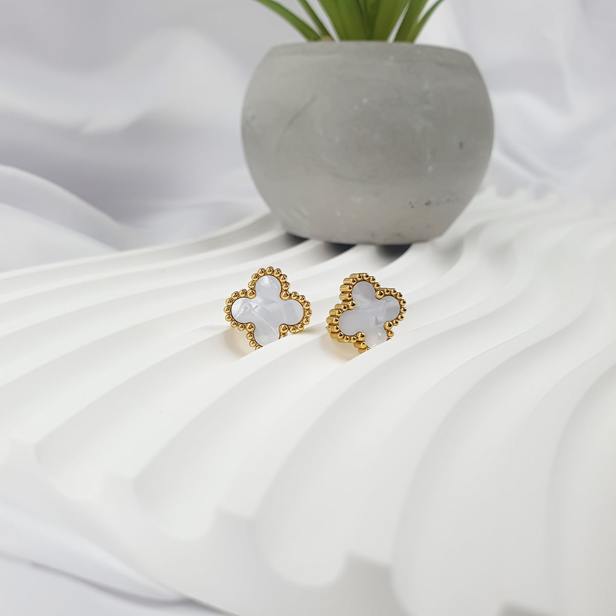 White enamel clover earrings at an angle on wavy white fabric