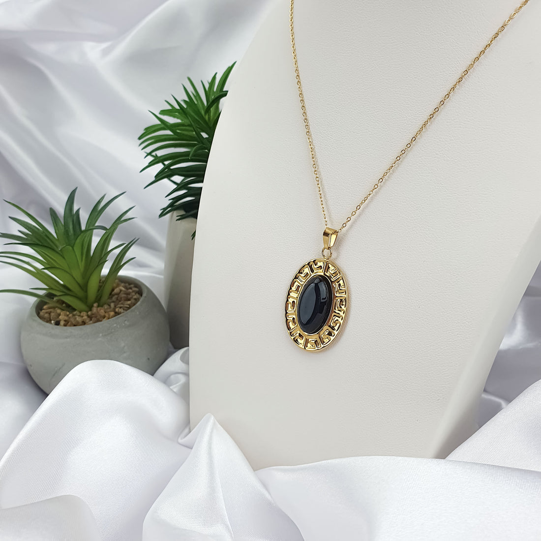 Necklace with a black oval stone in a meander frame on a white stand