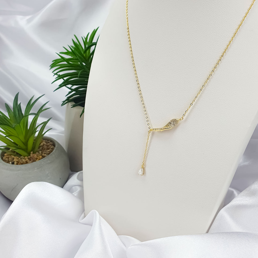 Necklace with a cubic zirconia wave and dangling teardrop on a white stand