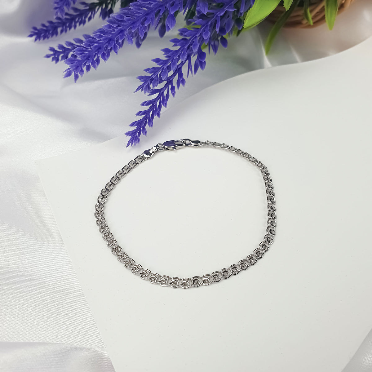 Silver-tone Love chain bracelet on a light surface beside violet flowers