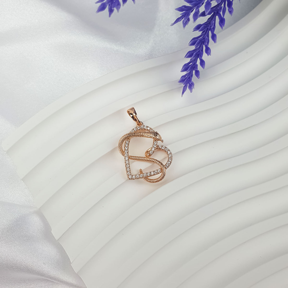 Gold-tone snake and heart pendant on white drapery with lavender