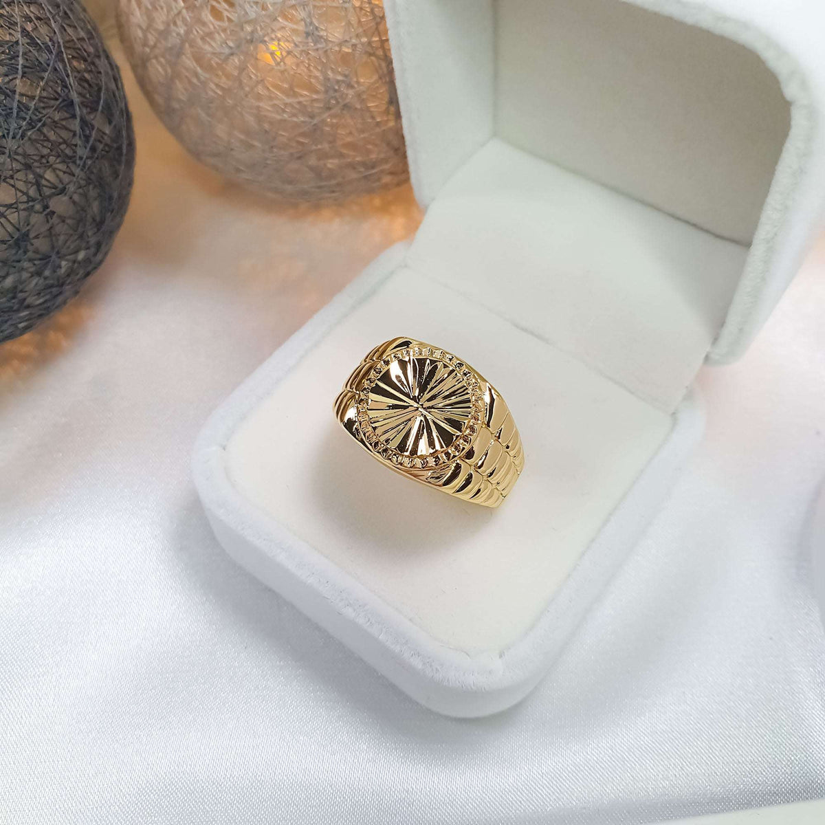 Gold-plated signet ring in a white gift box on light drapery