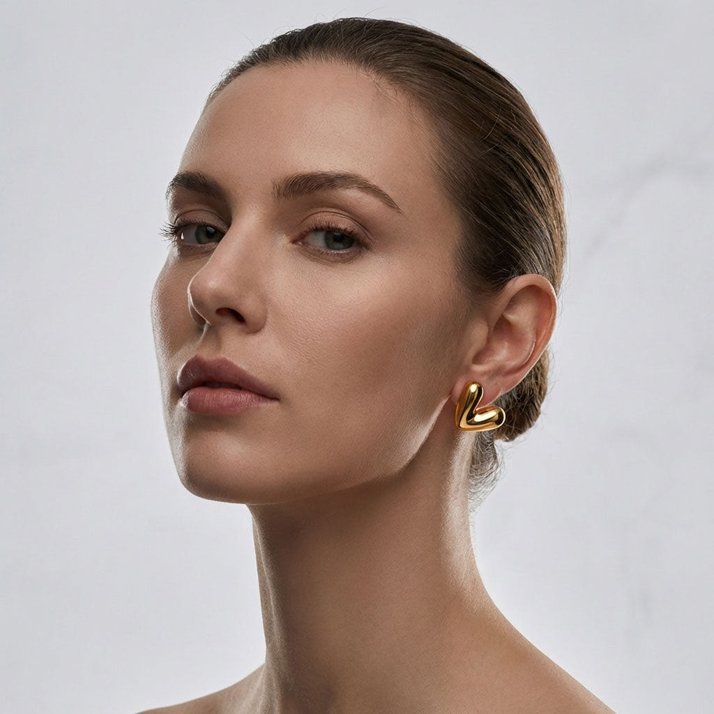 Close-up of a model wearing a gold-tone heart earring against a light background