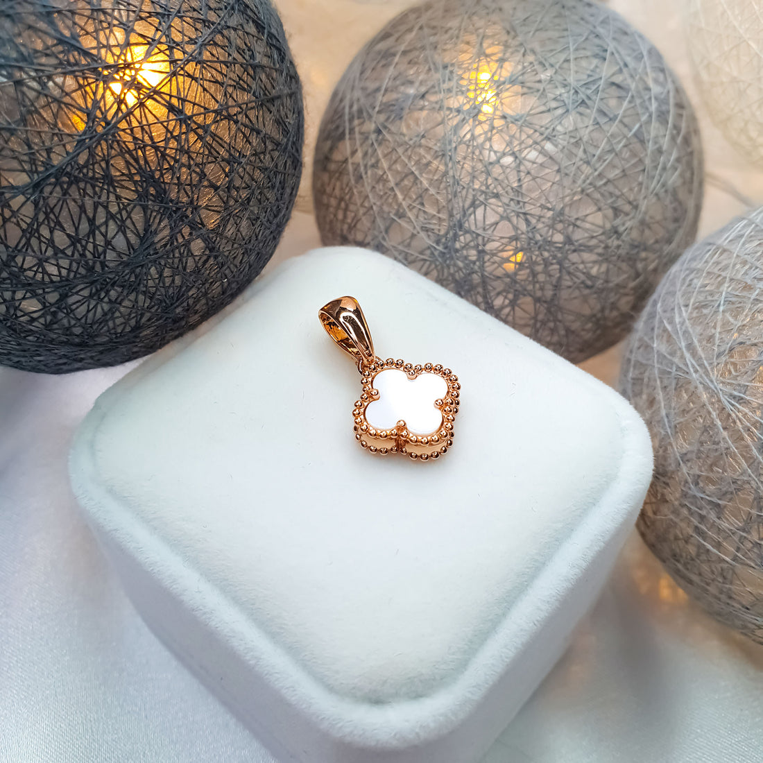 Gold-plated white clover pendant on a velvet box with decorative lights