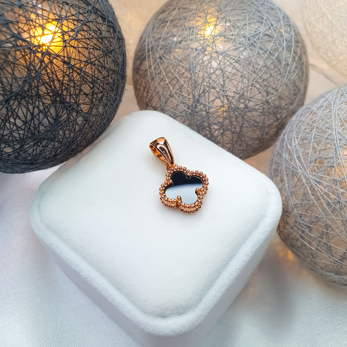 Black enamel clover pendant on a white velvet box, sparkling baubles behind